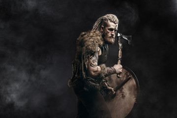 Medieval warrior berserk Viking with tattoo on skin, red beard and braids in hair with axe and...