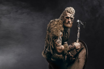 Medieval warrior berserk Viking with tattoo on skin, red beard and braids in hair with axe and...
