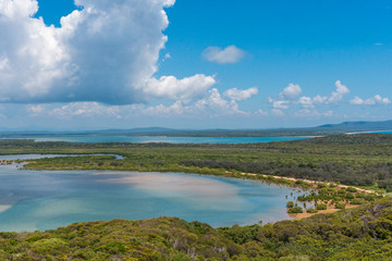 Fototapeta premium Untouched and lush forests covers the land, as it meets turquoise waters and bright yellow beaches on a cloudy and bright day near 1770 in Australia