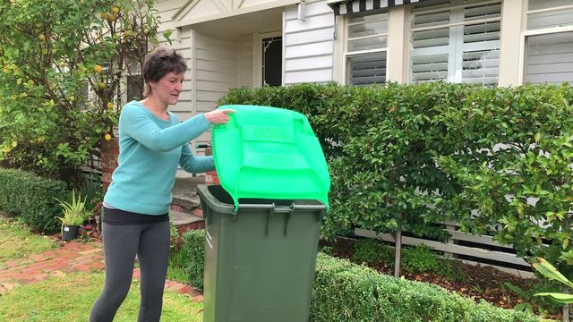 Mature woman putting garden clippings in garden green waste bin.