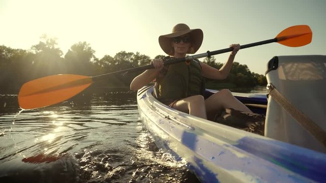 Girl In Kayak.Girl Traveller In Life Vest Swims In Kayak Boat In Tranquil Pond.Woman Exploring Calm River By Canoe.Pretty Woman In Hat And Sunglasses Kayaking On Lake At Sunset And Holds Oar Close Up 