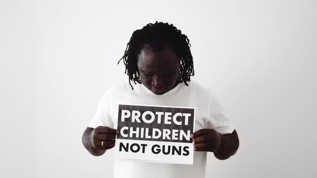 Black man with white T-shirt holding a sign Protect Children, Not Guns.