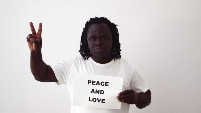 Serious black man in white t-shirt holds a sign Peace And Love.