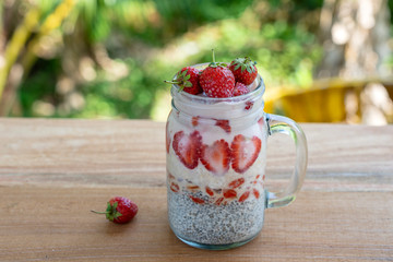 Almond milk chia pudding with fresh red strawberries, goji berries and oat flakes in a glass jar mug. Vegan raw breakfast. Chia seeds and fresh cut fruits and berries dessert