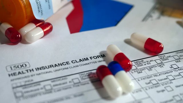 Prescription drug bottle and pills spilling onto a patient health insurance claim form.