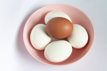 Group of organic clean surface a brown chicken egg and 4 white duck eggs put in pink melamine bowl. Background for healthcare or healthy food or modern kitchen concept.