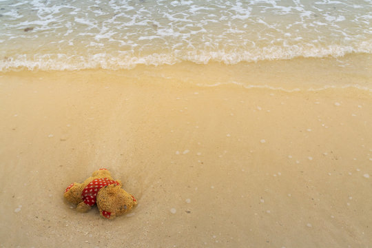Image of unwanted wet red cloth teddy bear doll and floating by the wave on dirty sand beach. Background for waste and garbage in ocean or pollution and environment problem in the sea.
