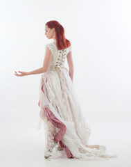 full length portrait of red haired girl wearing torn and tattered wedding dress. Standing pose...