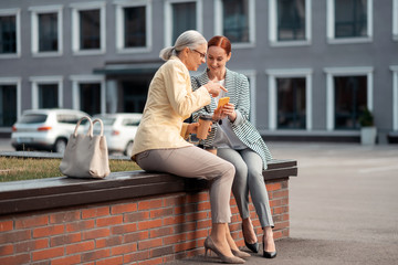 Obraz premium Pleased young businesswoman sitting with her colleague outdoors