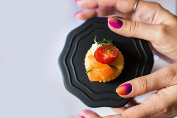 girl holds cracker cookies with red fish greens and tomato on a black plate with two hands