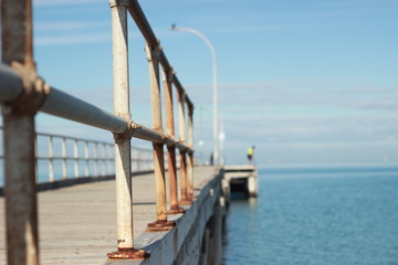 Fototapeta premium lone man standing on an old timber jetty hobby fishing on a sunny afternoon on the coast, Melbourne, Victoria, Australia