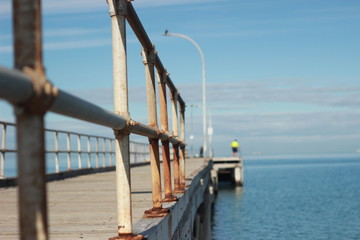 lone man standing on an old timber jetty hobby fishing on a sunny afternoon on the coast,...