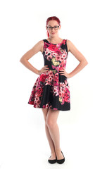 full length portrait of red haired girl wearing a cute flower patterned dress. Standing pose against a  white studio background.