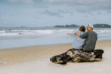 Asian senior couple or elderly people walking and siting at the beach on their weekend vacation holiday. Retirement vaction concept.