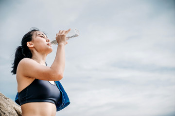 An beautiful Asian woman running and drinking some water during moring. Workout and sport outdoor concept.