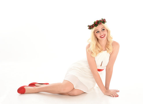 full length portrait of blonde girl wearing a white dress and flower crown.  Sitting pose, isolated against a  white studio background.