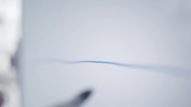 Close-up of a man's defocused hand drawing straight blue line on whiteboard