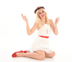 full length portrait of blonde girl wearing a white dress and flower crown.  Sitting pose, isolated against a  white studio background.