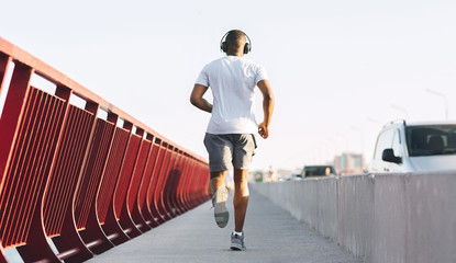 Sporty african american guy running along the bridge