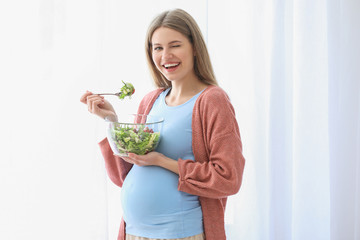 Beautiful pregnant woman eating salad at home