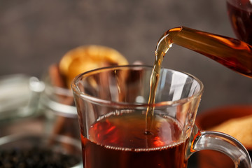 Pouring of hot tea in cup on table, closeup