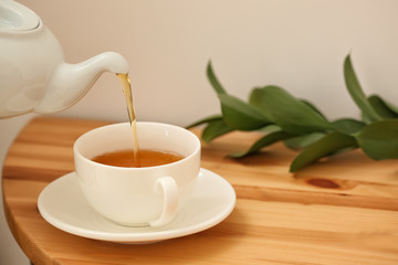 Pouring of hot tea in cup on table
