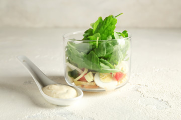 Glass with tasty arugula salad and sauce on light table