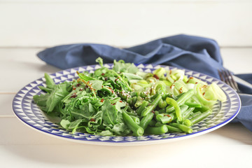Plate with tasty arugula salad on table