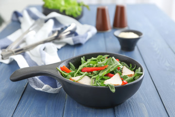 Bowl with tasty arugula salad on wooden table
