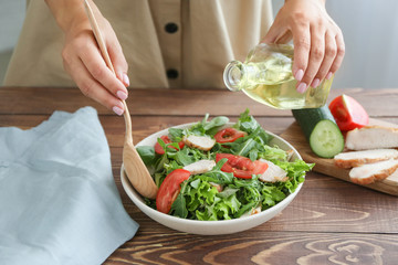 Obraz na płótnie Canvas Woman preparing tasty arugula salad on table, closeup