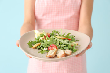 Woman holding plate with tasty arugula salad on color background, closeup