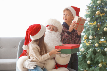Santa Claus and little children with gifts in room decorated for Christmas