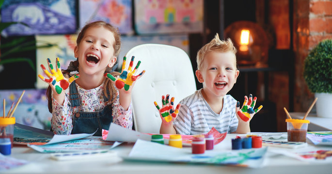 funny children girl  and boy draws laughing shows hands dirty with paint.