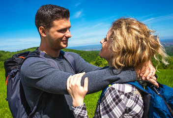 Young couple enjoying hiking together in nature standing on the top of the hill.