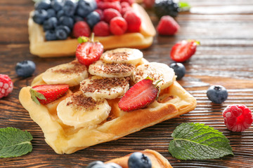 Tasty sweet waffles with fruits on wooden table
