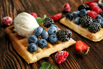 Tasty sweet waffles with berries and ice cream on wooden table