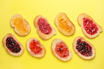 Tasty toasted bread with different jams on color background