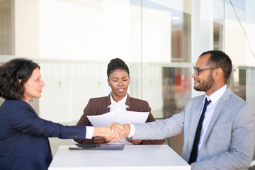 Two business partners closing deal, while legal expert explaining contract details. Multiethnic business man and women sitting at table, checking papers and shaking hands. Agreement concept