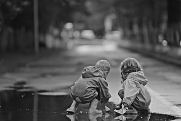 brother and sister play boats in a puddle / raincoats clothes, autumn weather children play paper boats