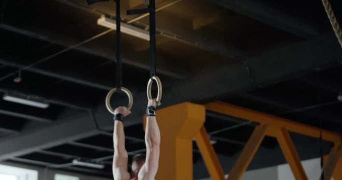 Man in Gym performs pull-ups on gymnastic rings, crossfit training day.