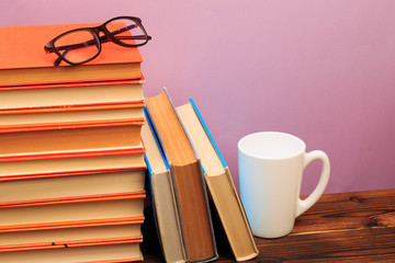  pile of old books with mug ang glasses  panorma, good copy space  on pink background