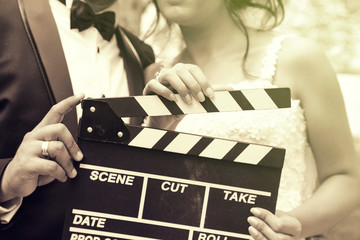 Happy beautiful bride and groom, woman holds clapper board, cinema board 
