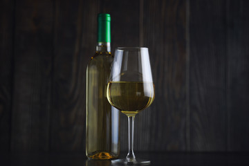 Transparent bottle of white dry wine on the table. White wine glass on a wooden background.