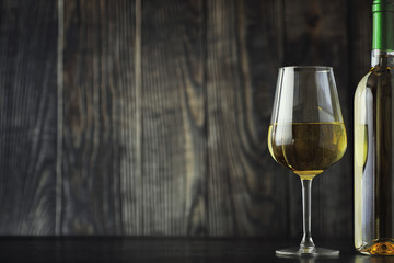 Transparent bottle of white dry wine on the table. White wine glass on a wooden background.