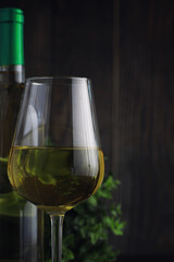 Transparent bottle of white dry wine on the table. White wine glass on a wooden background.
