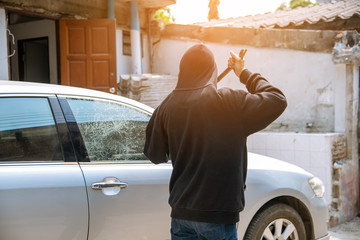Car thief stealing to break glass into a car .Masked hide face man ,robber dressed in black holding crowbar into car damage glass window of car.