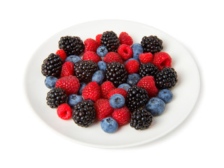 ripe fresh berries of blackberry, blueberry and raspberry berries in a white plate isolated on white background