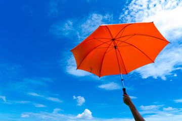 The man holding orange umbrella in bottom view for protect skin from the sun, high uv on the blue summer sky with white fluffy clound. Freedom in the blue sky.
