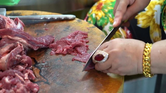 Traders are slicing pork on a butcher in a bazaar.