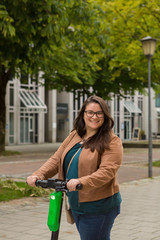 Naklejka premium Young lady poses while riding an electric scooter in the city.